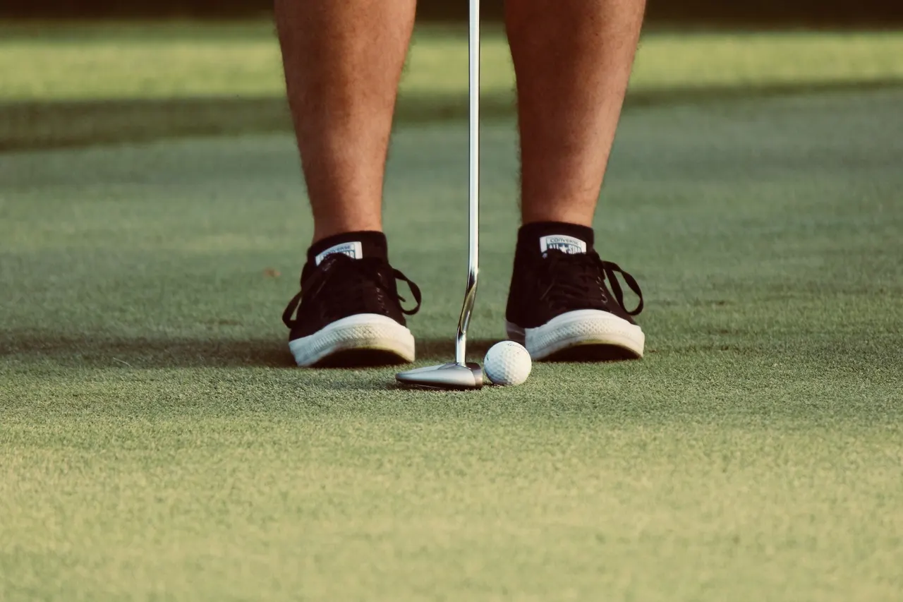 Golfer's feet with a golf ball and club positioned for putting.