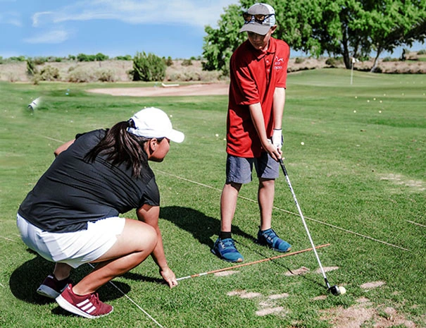 Boy Holding Golf Club in Front of Crouching Woman